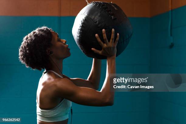 side view of woman holding medicine ball while listening music against wall in gym - medicine ball stock pictures, royalty-free photos & images
