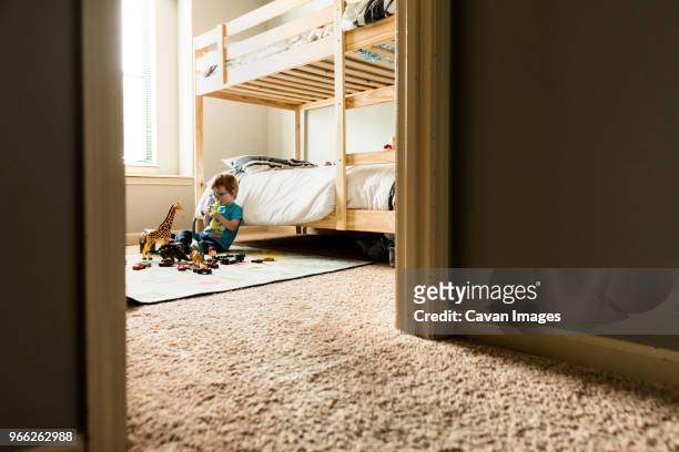 boy playing with toys in bedroom seen through doorway - alleen kinderen stockfoto's en -beelden