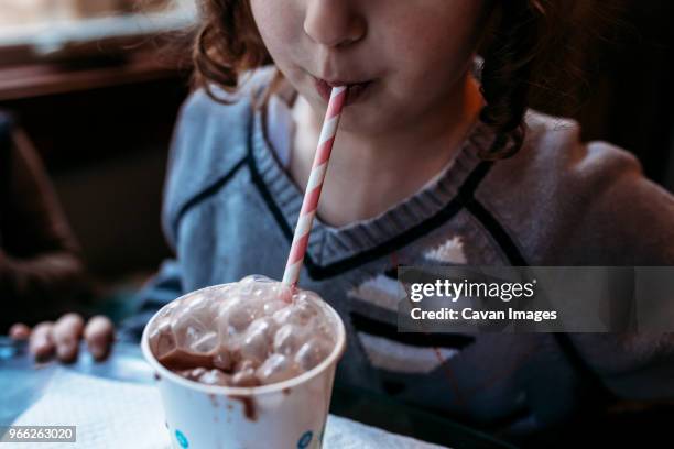midsection of playful girl blowing bubbles in chocolate milk at home - drinking straw stock-fotos und bilder