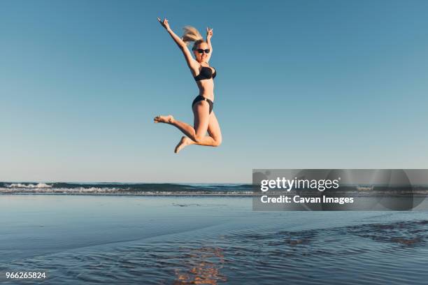 carefree woman jumping at beach against clear sky - bibione stock pictures, royalty-free photos & images