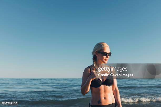 thoughtful woman wearing bikini and sunglasses against sea and clear sky - bibione stock pictures, royalty-free photos & images
