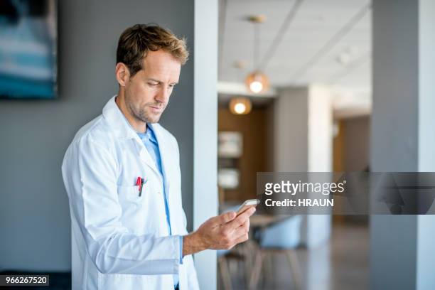 confident doctor using mobile phone in hospital - homens de idade mediana imagens e fotografias de stock