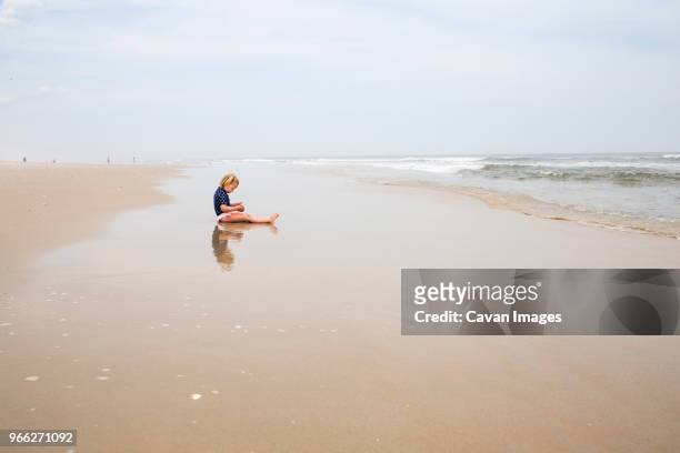 side view of girl playing while sitting on shore at beach against sky - westminster maryland stockfoto's en -beelden
