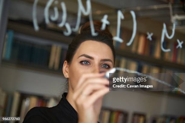 businesswoman writing formula on glass wall at office - mathematics stock pictures, royalty-free photos & images
