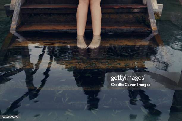 low section of woman taking fish pedicure while standing on steps in lake - garra rufa fish stock pictures, royalty-free photos & images