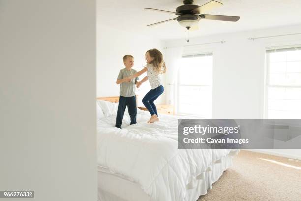 siblings holding hands while jumping on bed - jump on bed photos et images de collection