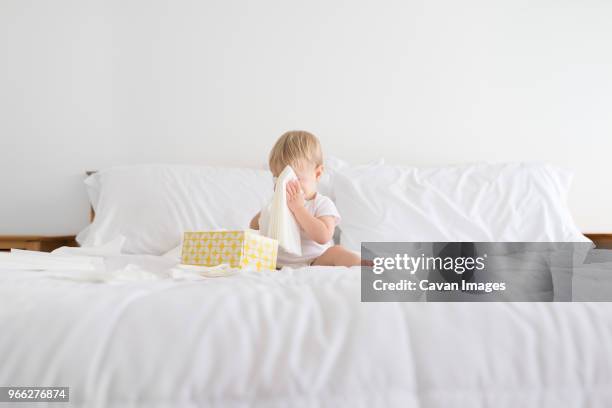 boy hiding face with facial tissue while playing on bed at home - handkerchief stock pictures, royalty-free photos & images