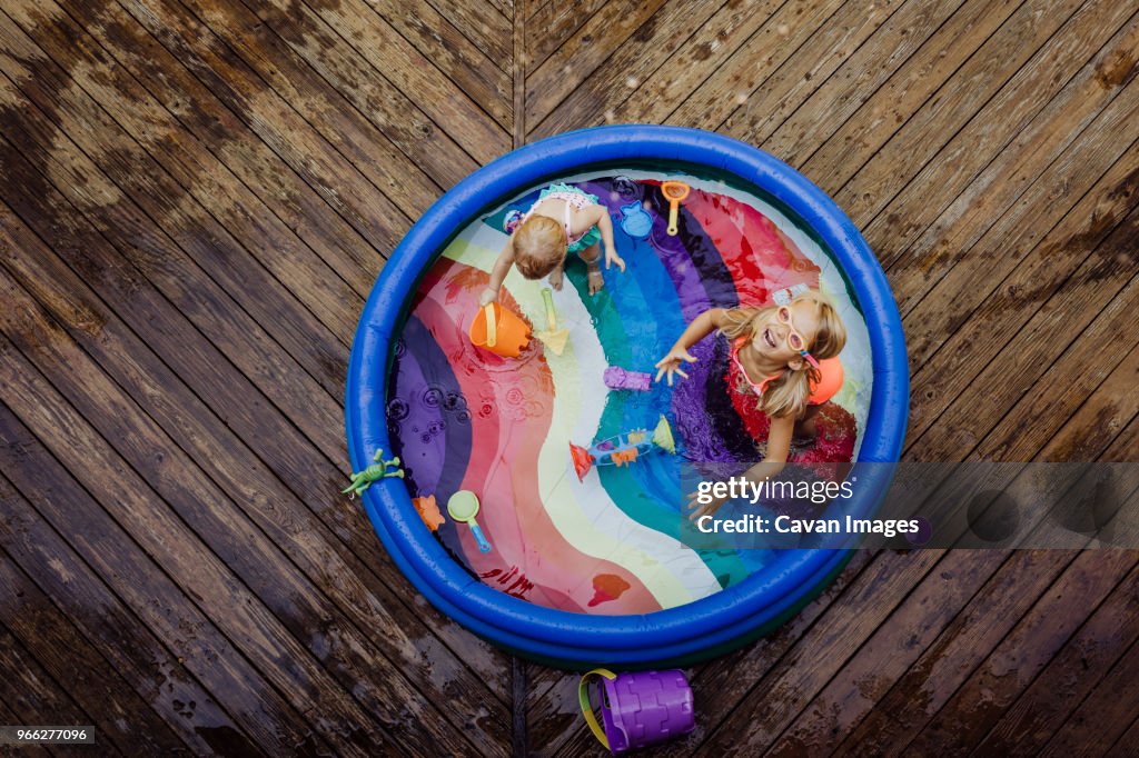 High angle view of sisters playing in wading pool on wood