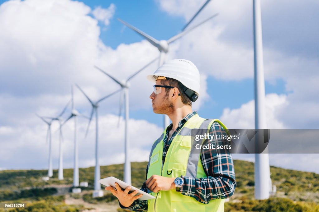 Young engineer man looking and checking wind turbines at field