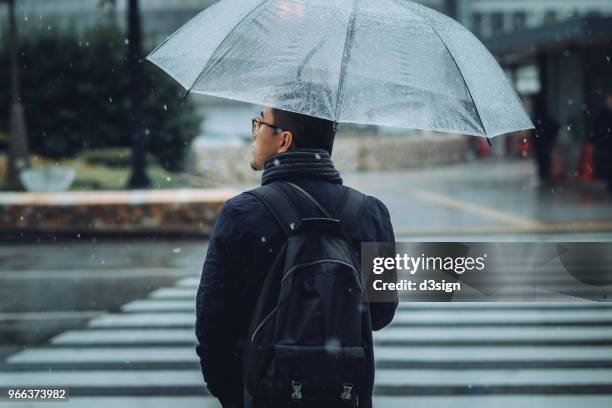 rear view of man with umbrella walking in city in snow during winter - リュックサック ストックフォトと画像