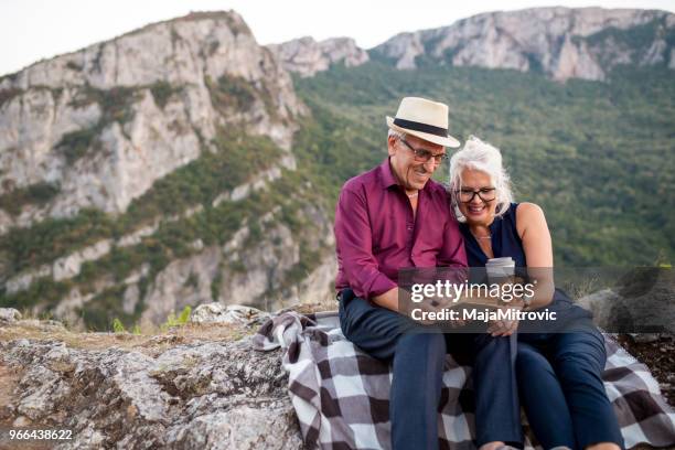 loving senior couple hiking, sitting on the top of rock, exploring. active mature man and woman hugging and happily smiling. - woman sitting top man stock pictures, royalty-free photos & images