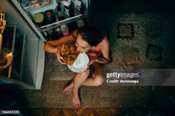 mujer comer delante de la nevera en la cocina de noche - hora del día fotografías e imágenes de stock