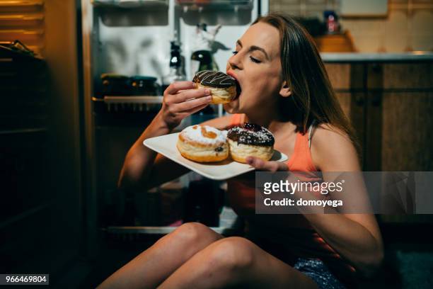 donna che mangia ciambelle davanti al frigorifero a tarda notte - eating donuts foto e immagini stock