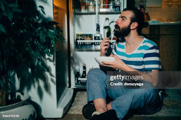 junger mann essen spät in die nacht vor dem kühlschrank - mitternacht stock-fotos und bilder