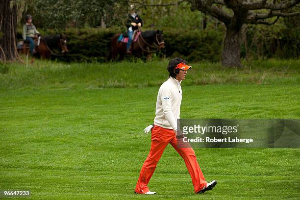Ryo Ishikawa of Japan walks on the 13th fairway as two people ride their horses in the background during a practice round for the AT&T Pebble Beach...