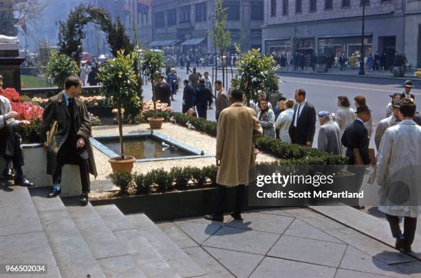 New York City - View of pedestrians on Madison Avenue gathered around a an artificial garden and pond on the steps of an unspecified office building.