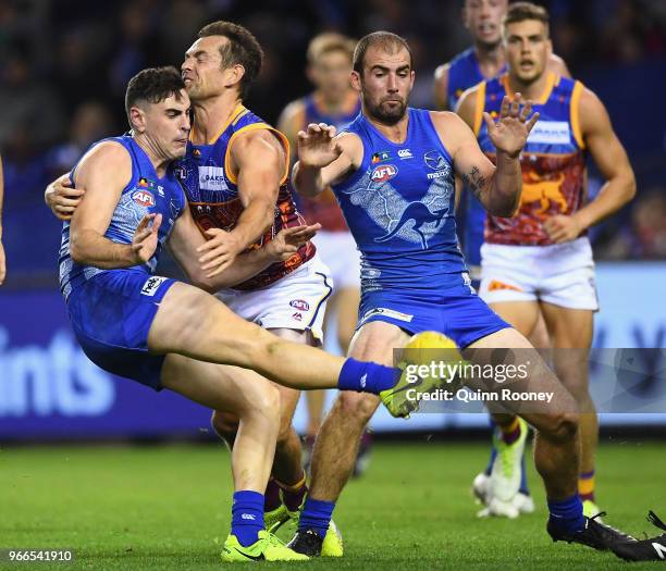 Paul Ahern of the Kangaroos kicks whilst being tackled by Luke Hodge of the Lions during the round 11 AFL match between the North Melbourne Kangaroos...
