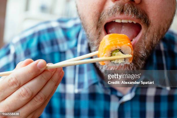 close up view of man with beard eating sushi roll with salmon using chopsticks - chopsticks stock pictures, royalty-free photos & images