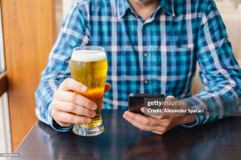 Man drinking beer and using mobile phone in a bar