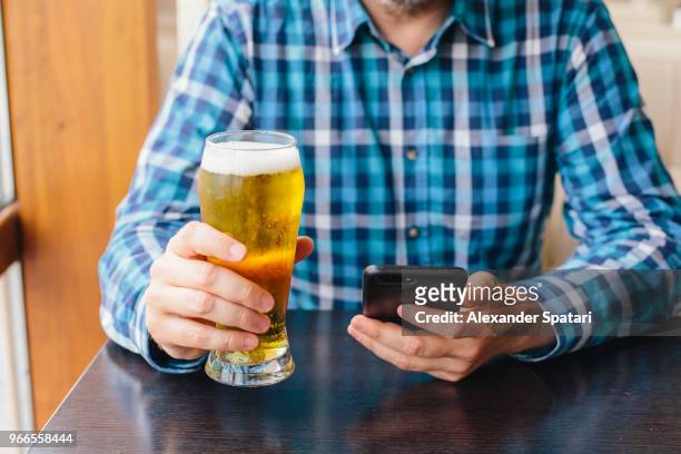 man drinking beer and using mobile phone in a bar - holding beer stock pictures, royalty-free photos & images