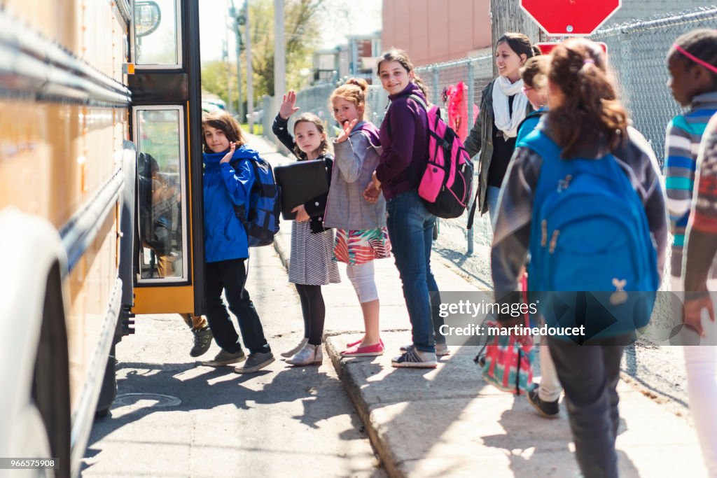 Kids in line waiting to get on school bus saying goodbye.