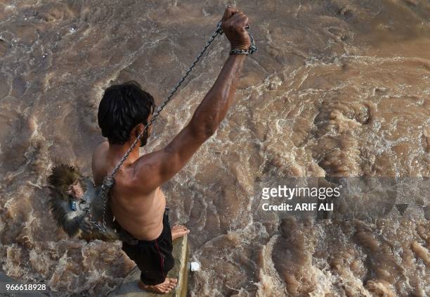 Pakistani man carries a monkey as he tries to jump in a canal during a hot summer day in Lahore, on June 3, 2018.