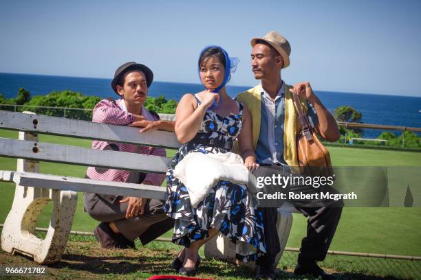 dressed in retro fashions, a young australian-chineseapproaches a young asian couple, to express a sexual interest in the husband, as he sits on a park bench with his wife, outside a bowling club, overlooking the ocean, on a hot, sunny summer's afternoon. - 1961 stock pictures, royalty-free photos & images