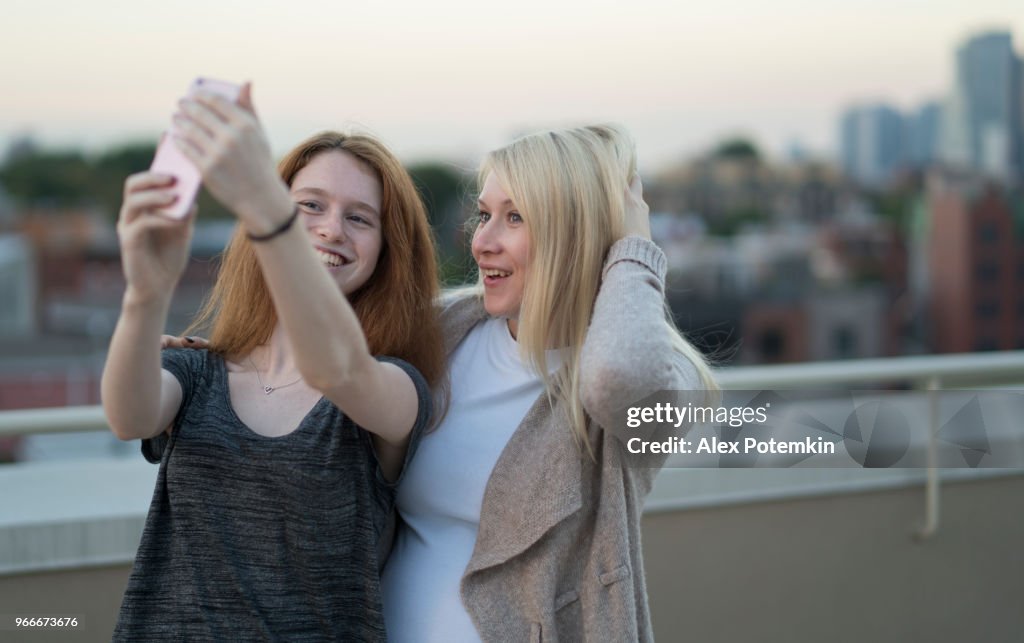 Die junge ziemlich schwanger Frau mit ihrer kleinen Schwester, der 16 Jahre alten Teenager Mädchen, zusammen hängen, Selfies fotografieren mit dem Smartphone und Spaß auf dem Dach