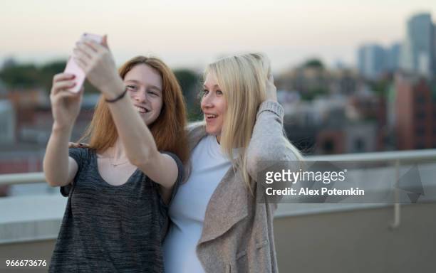 die junge ziemlich schwanger frau mit ihrer kleinen schwester, der 16 jahre alten teenager mädchen, zusammen hängen, selfies fotografieren mit dem smartphone und spaß auf dem dach - 25 29 years stock-fotos und bilder