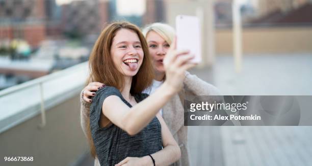 die junge ziemlich schwanger frau mit ihrer kleinen schwester, der 16 jahre alten teenager mädchen, zusammen hängen, selfies fotografieren mit dem smartphone und spaß auf dem dach - 25 29 years stock-fotos und bilder