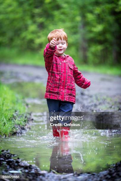 young cute kid walking jumping into water puddle - onfokus stock pictures, royalty-free photos & images