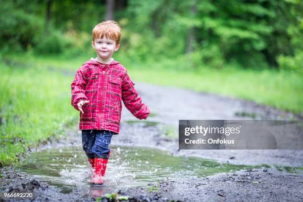 young cute kid walking jumping into water puddle - onfokus stock pictures, royalty-free photos & images