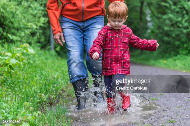 young cute kid walking jumping into water puddle with dad - onfokus stock pictures, royalty-free photos & images