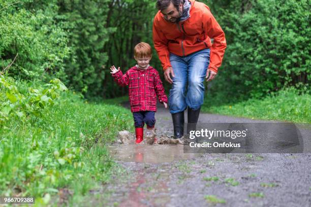 young cute kid walking jumping into water puddle with dad - onfokus stock pictures, royalty-free photos & images