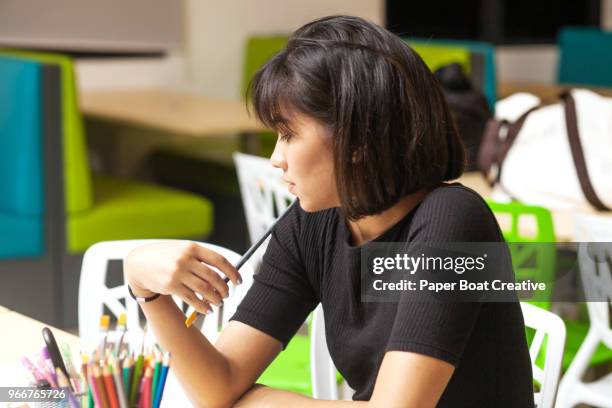 young woman thinking of what she will draw next, while sitting in a creative office - タギグ ストックフォトと画像