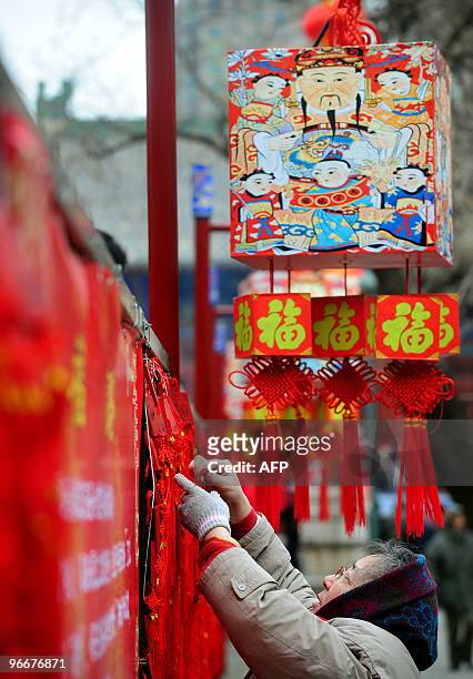 Woman hangs a lucky votive offering beneath a display of hanging ornamnets featuring the God of wealth on the first day of the Chinese new year at...