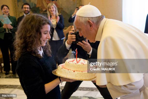Le pape François souffle une bougie posée sur un gateau offert par une jeune fille de l'Action Catholique Italienne le jour anniversaire de ses 79...
