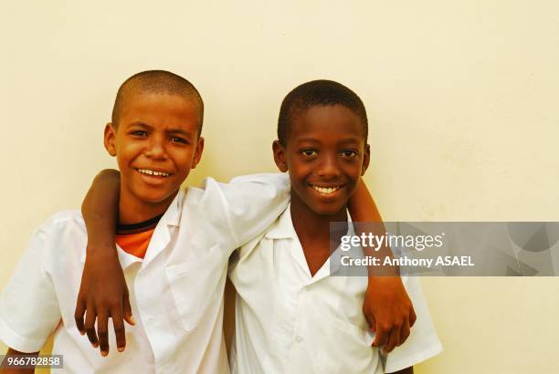 Mauritius, Trou Aux Biches, cheerful young school boys enjoying together while standing in front of wall with arms around.