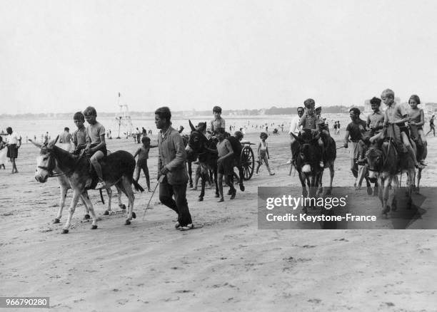 Des touristes et des enfants à dos d'âne sur la plage le 26 août 1938 à La Baule, France.