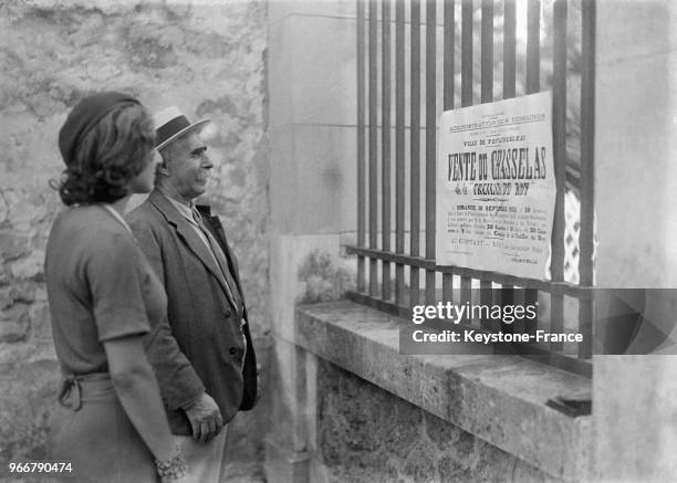 Un homme et une femme lisent l'affiche annonçant la vente aux enchères du célèbre raisin chasselas de la treille du Roy, à Fontainebleau, France le...