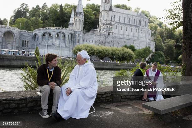 Priest talking with young pilgrim with the Basilica of the Immaculate Conception in the background pictured in Lourdes, France on August 13, 2010.
