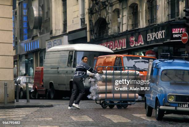 Travailleur immigré poussant un chariot de rouleaux de tissu dans le quartier du Sentier le 13 novembre 1989 à Paris, France.