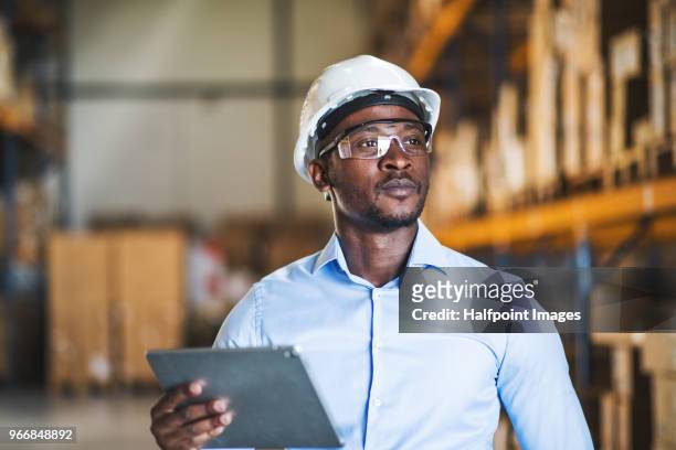 mature man manager or supervisor with clipboard in a warehouse. - black helmet stock pictures, royalty-free photos & images