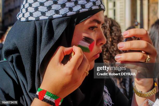 Femme voilée se mettant du maquillage aux couleurs du drapeau palestinien lors d'un rassemblement devant l'Hotel de ville en signe de solidarité avec...