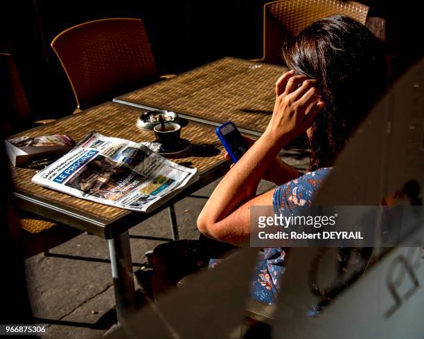 Une cliente en terrasse d'un bistrot prend un café en regardant son téléphone portable, le journal Le Progrès posé sur la table, quartier...