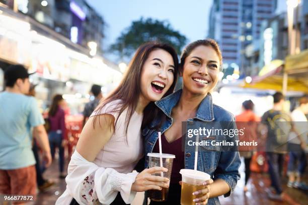 two malaysian woman with drinks at a night market - malaysian culture stock pictures, royalty-free photos & images