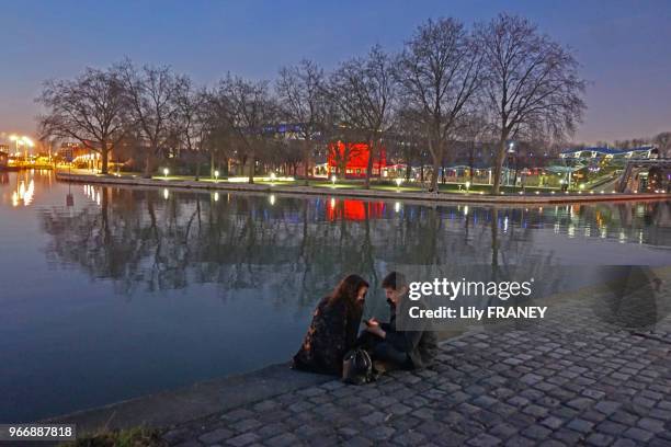 Couple assis sur le quai du canal de l'Ourcq à la nuit tombante, 17 février 2017, Paris, France.