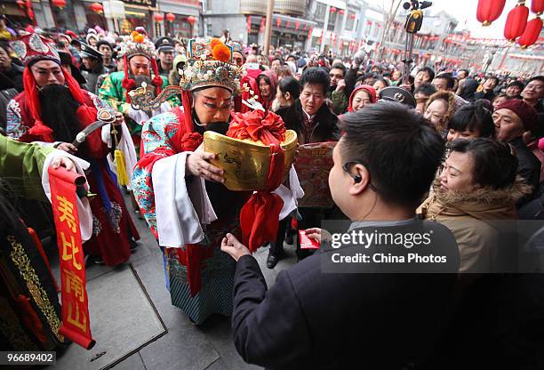 An actor dressed as the God of Fortune presents an ornament in the shape of gold ingot to businessmen of a shop for luck at the Qianmen Avenue during...