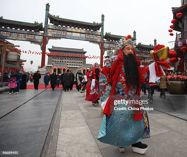 An actor dressed as the God of Fortune holding an ornament in the shape of gold ingot walks through shops for luck at the Qianmen Avenue during...