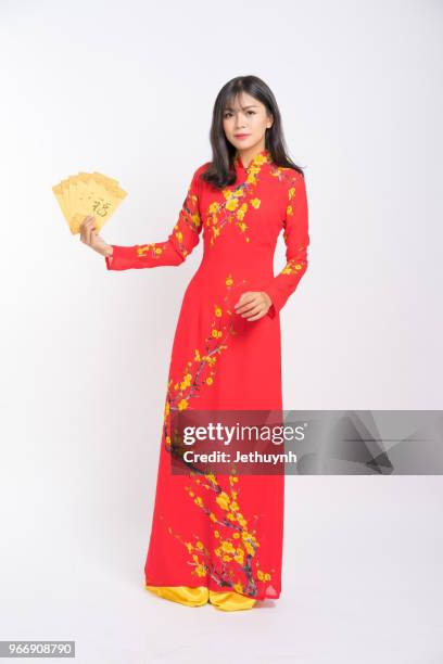 young woman wearing vietnamese red color ao dai, smiling, holding yellow envelope lucky packet - ao dai stockfoto's en -beelden